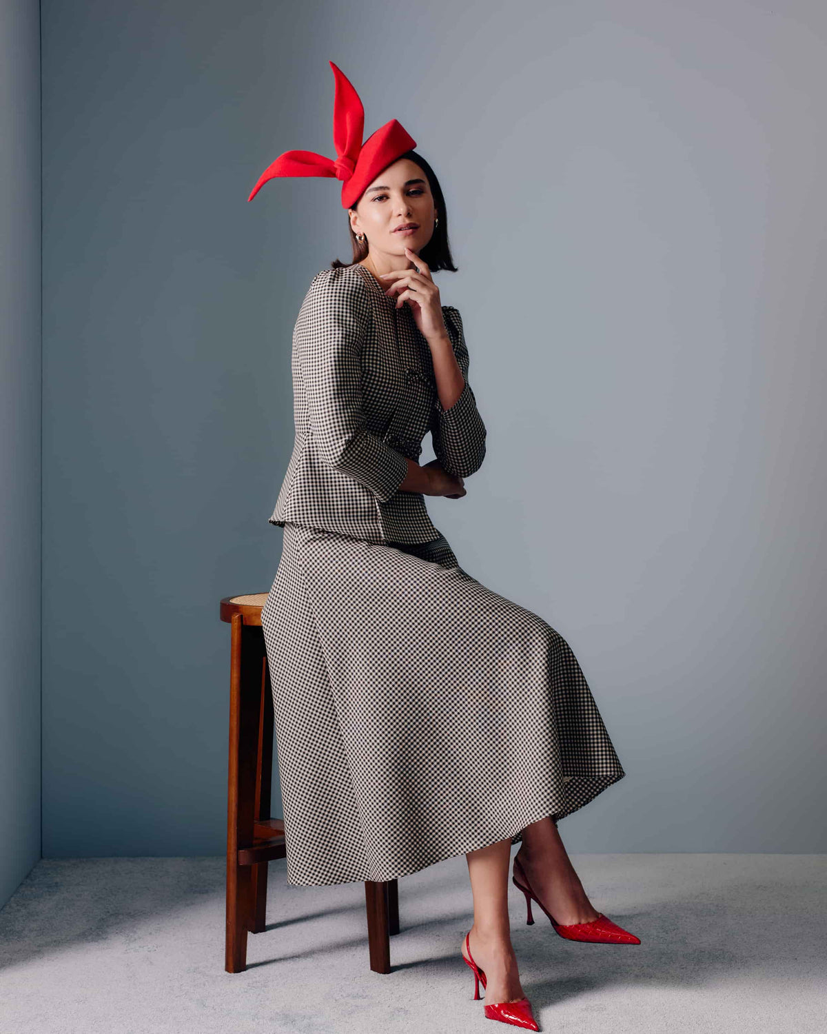 Couture red velour felt percher hat with a rounded base and a sculptural bow at the top.