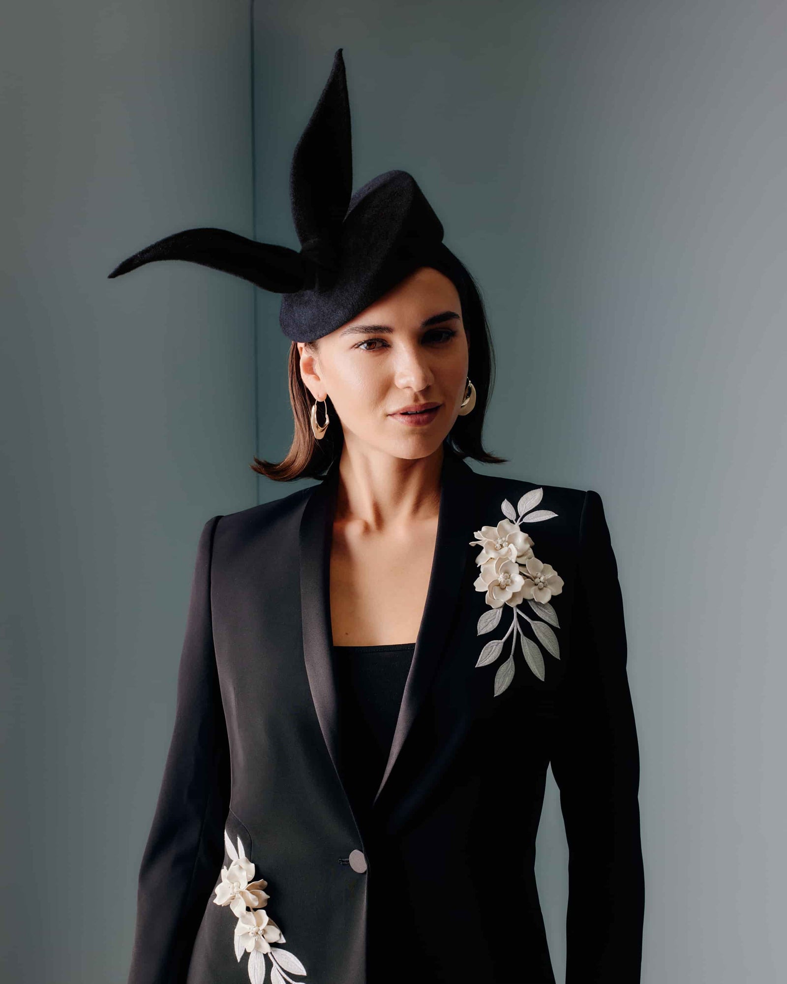 Couture black velour felt percher hat with a rounded base and a sculptural bow at the top.